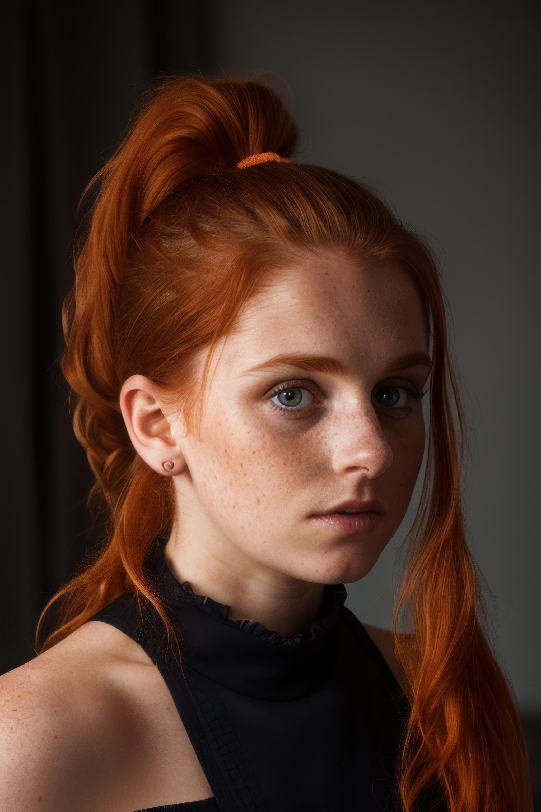 A teenage girl with bright red hair and a ponytail is looking directly at the camera.